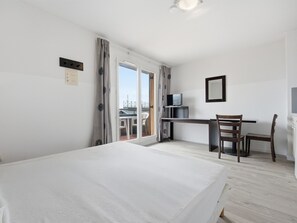 Ein Hotelzimmer mit Bett, Schreibtisch mit Fernseher, Stuhl und einem Balkon mit Aussicht.