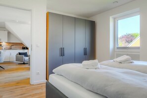 A bedroom with a large wardrobe, a bed with white linens, and a view of the outdoors through a window. - Wind Force 7/5, Grömitz. Sauna. Balcony. Meernah. (Grömitz)