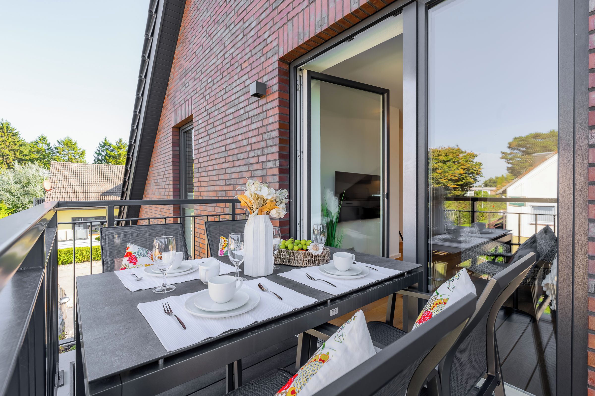 An outdoor dining area with a table set for two, a brick wall, and a sliding glass door leading to a balcony.