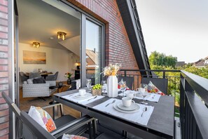 An outdoor dining area with a table set for two, a sofa, and a chair, with a view of the neighborhood. - Wind Force 7/5, Grömitz. Sauna. Balcony. Meernah. (Grömitz)