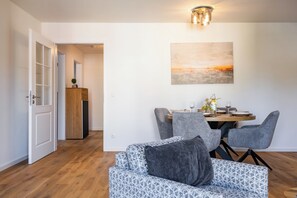 A modern living room with a dining area, wooden flooring, and a painting on the wall. - Wind Force 7/5, Grömitz. Sauna. Balcony. Meernah. (Grömitz)
