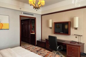 A hotel room with a bed, desk, television, and artwork on the wall.