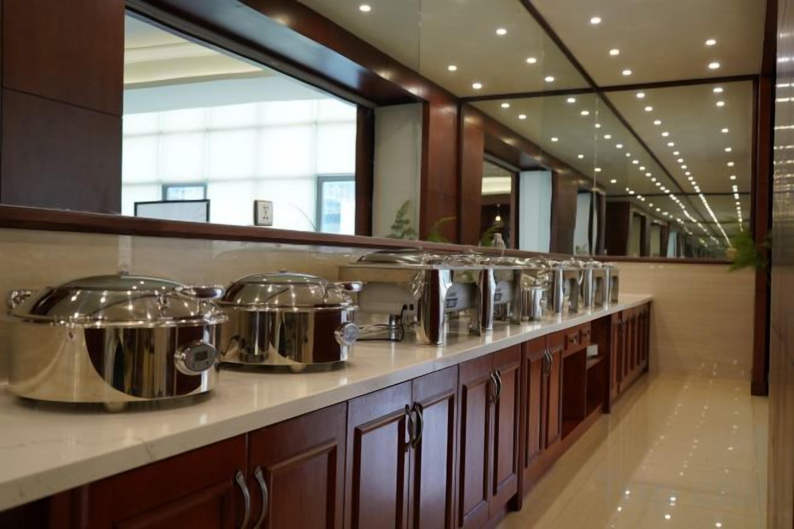 A buffet setup with multiple food service stations, a polished marble countertop, and a reflective ceiling.