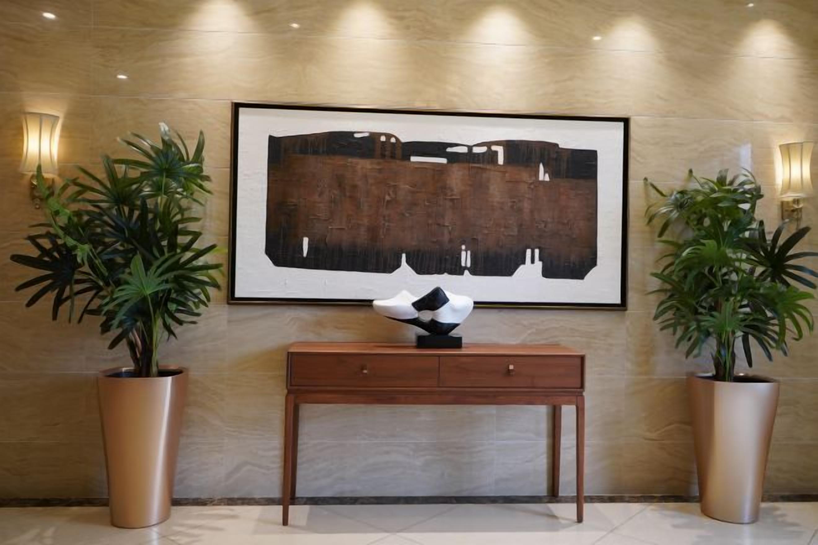 Un hall con una obra de arte grande enmarco, una consola de madera y dos plantas en macetas.