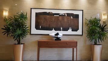 Un hall con una obra de arte grande enmarco, una consola de madera y dos plantas en macetas.
