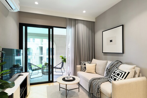 Un salon moderne avec un canapé, une table basse et un téléviseur. Une porte-fenêtre coulissante donne accès à un balcon extérieur.