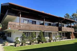 A two-story building with a balcony, potted plants, and a grassy lawn. - Apartment Unterbergblick (Reit im Winkl)