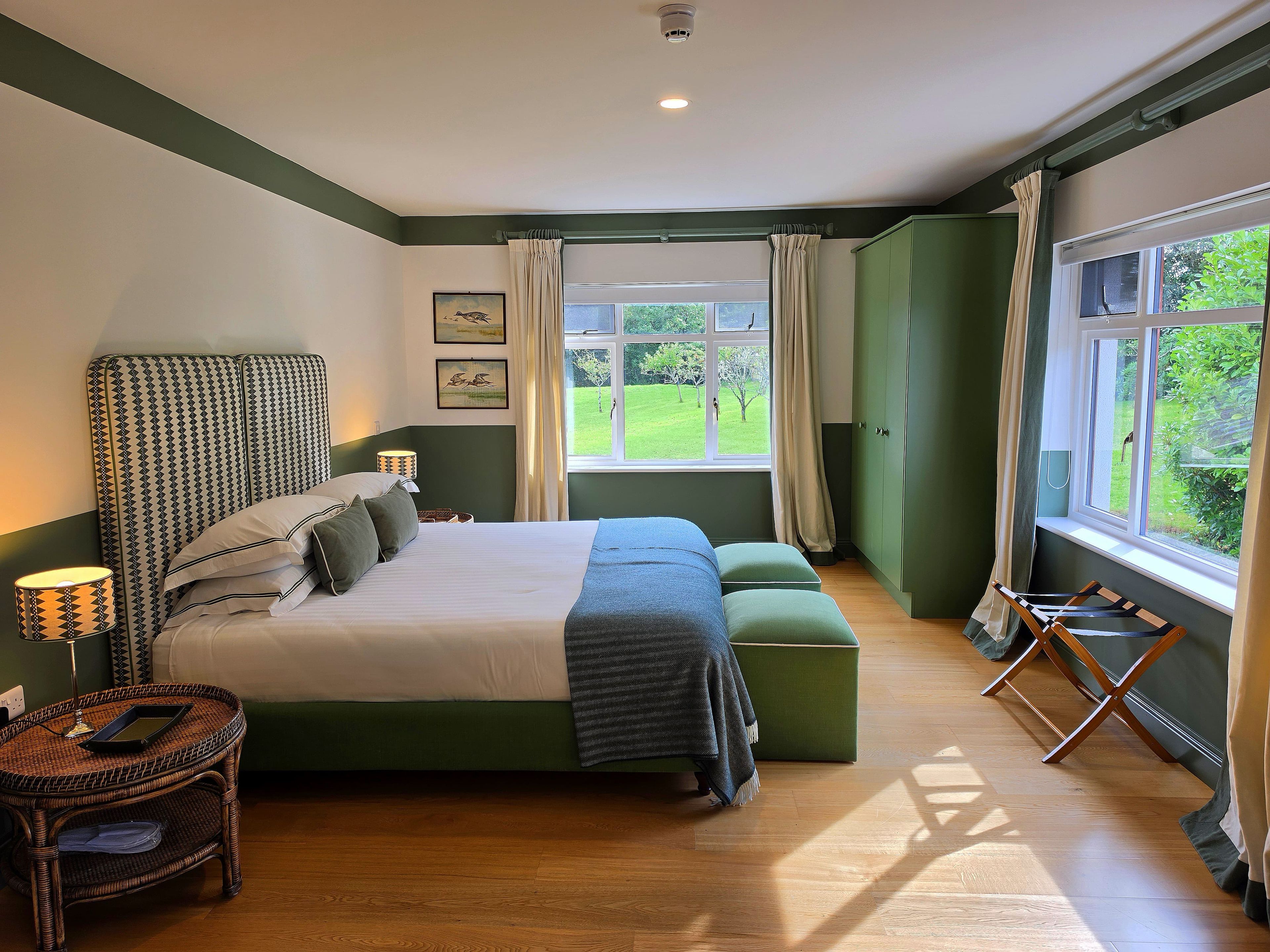 Un dormitorio con una cama grande, un sofá verde, una mesita de mimbre y una ventana con vistas a zonas verdes.
