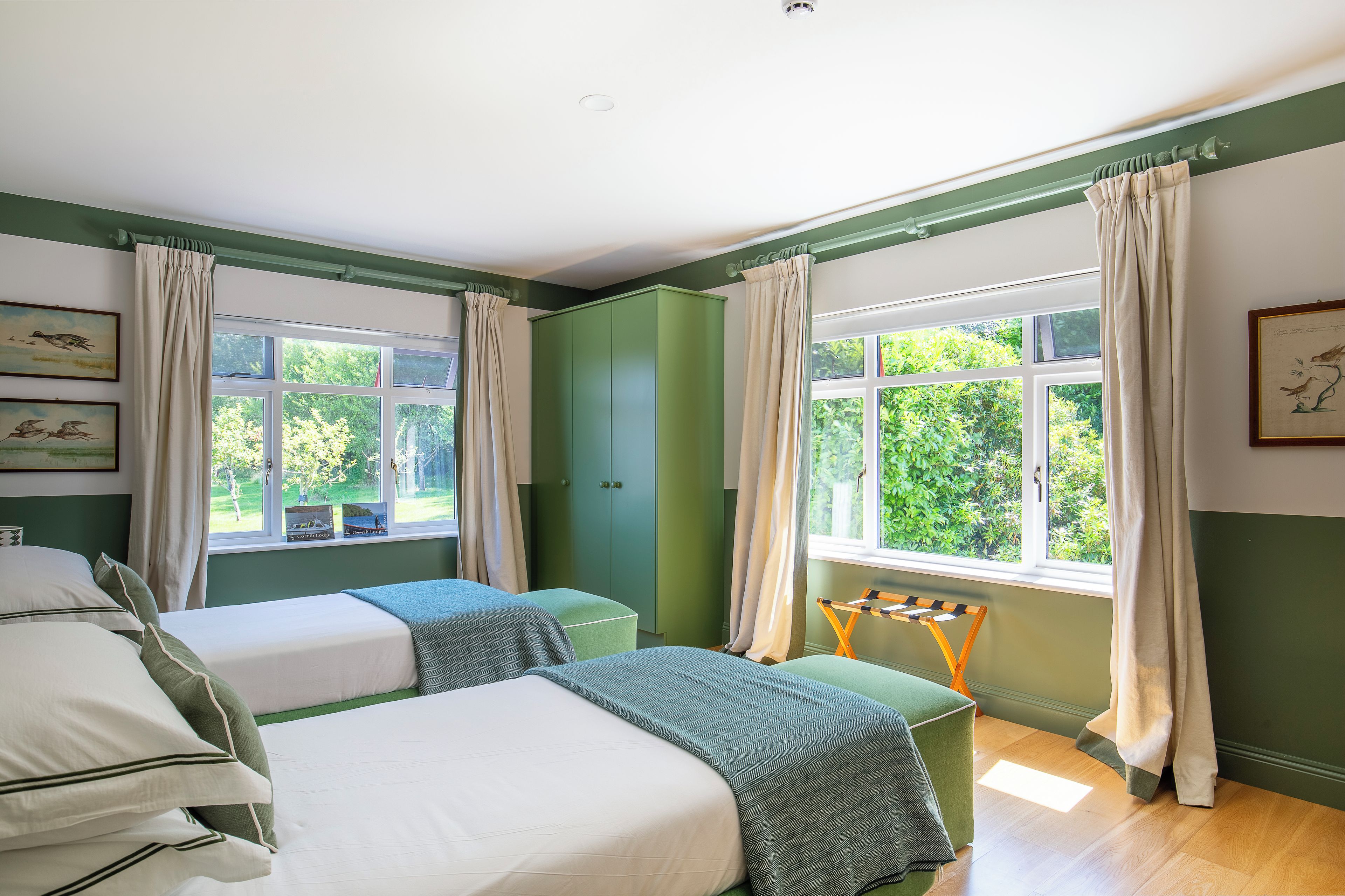 A room with two beds, a green wardrobe, and a window with curtains.