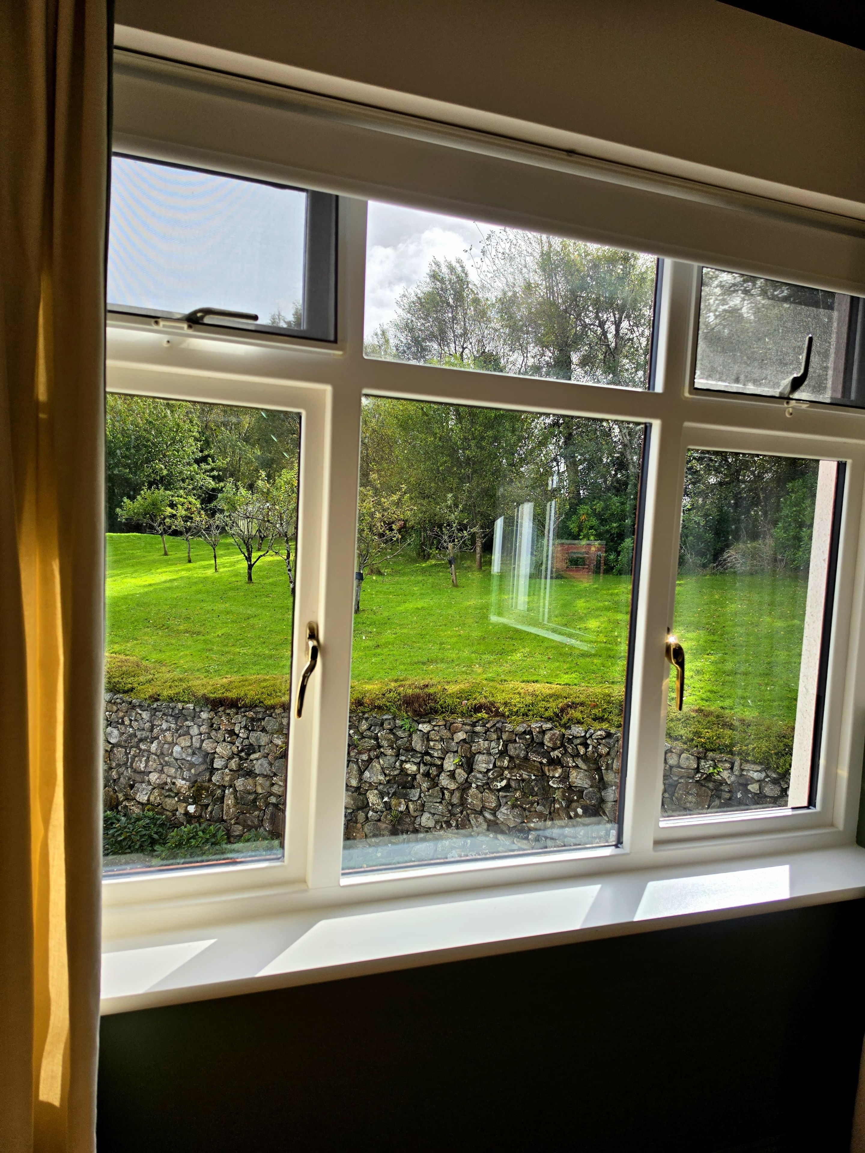 A window with a view of a grassy yard and a stone wall.