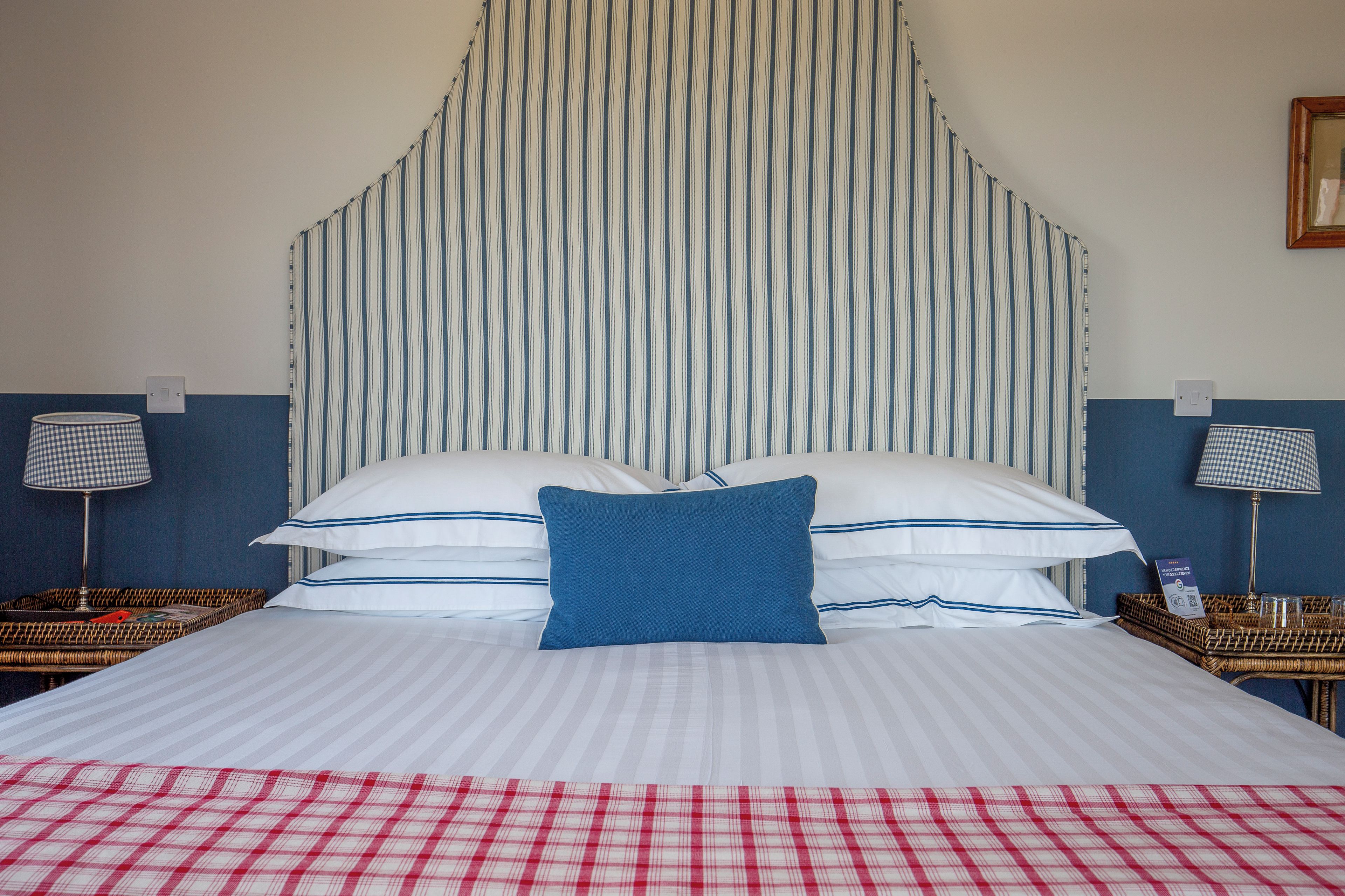 A hotel room with a large bed, striped headboard, two bedside tables with lamps, and a checkered throw on the bed.