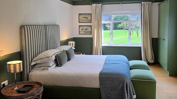 Un dormitorio con una cama grande, una mesita de noche con lámpara, una ventana con cortinas y vistas a un paisaje verde.