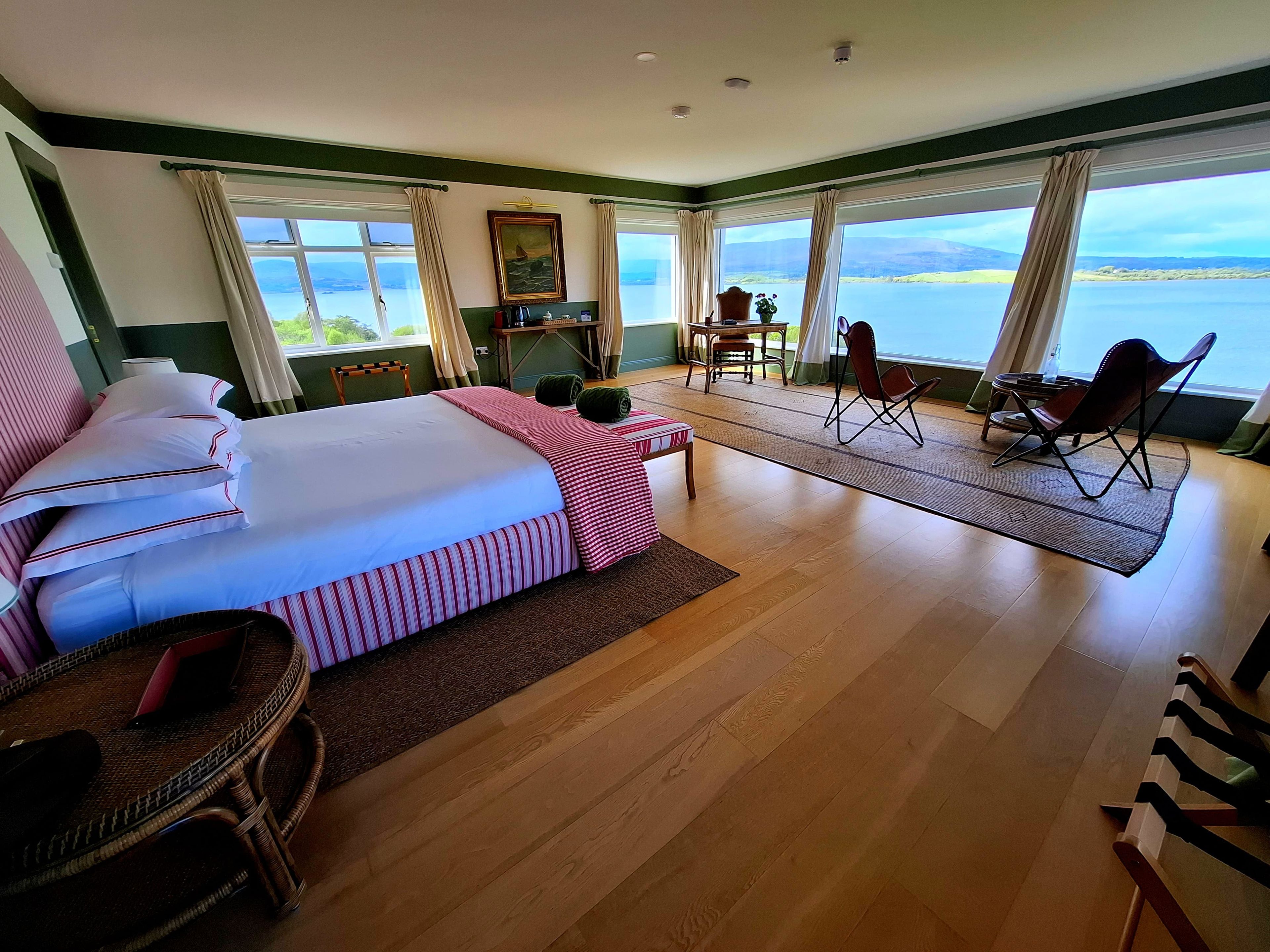 Habitación de hotel con una cama grande, un comedor con sillas y vista al mar.