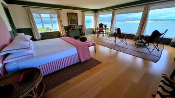Habitación de hotel con una cama grande, un comedor con sillas y vista al mar.