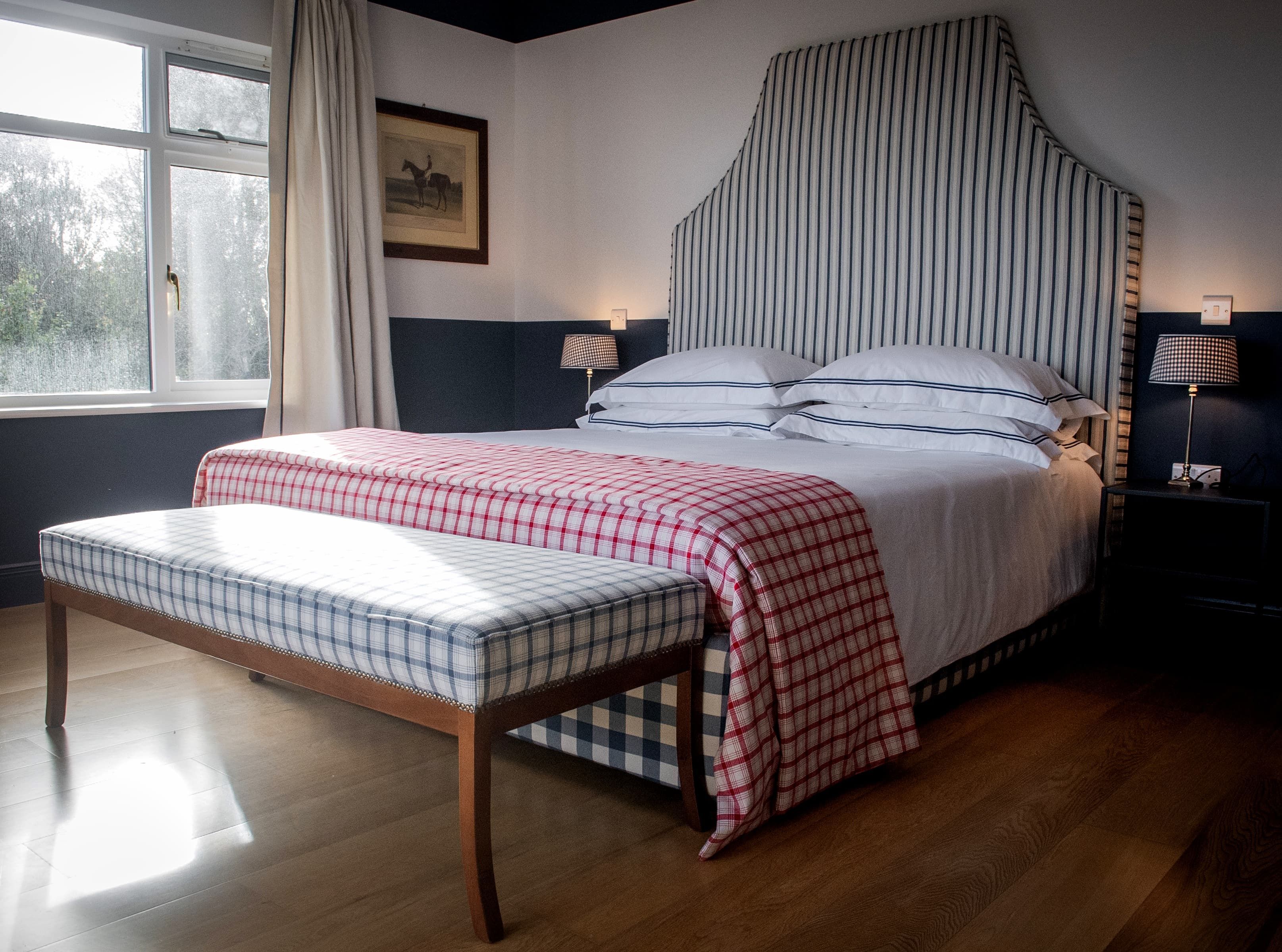 A bedroom with a bed, bedside tables, a window with curtains, and a framed picture on the wall.