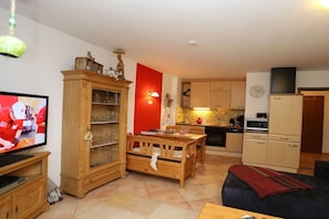 Ein Wohnzimmer mit Fernseher, Holzmöbeln, einer Küchenzeile inklusive Schränken und Mikrowelle sowie einer roten Akzentwand.