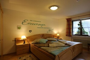 Ein Schlafzimmer mit einem Bett, Nachttischlampen, einer Wand mit einem Zitat und einem Fenster mit Vorhängen.