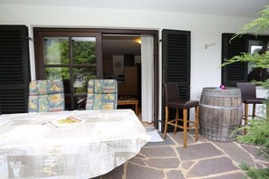 An outdoor seating area with a table and chairs, a wooden barrel, and a view through a door into a room. - Holiday apartment with 1 bedroom (Grainau)