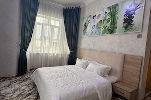 A hotel room with a large bed, a wooden headboard, a nightstand, and a window with blue curtains.