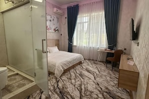 Una habitación de hotel con cama, escritorio, silla, ducha y televisión.