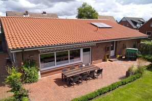 Ein Wohnhaus mit Ziegeldach, einer überdachten Terrasse mit Tisch und Stühlen und einer Ziegelaußenwand.