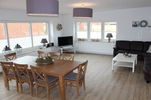 A modern living room with a dining area, large windows, a fireplace, and a black leather sofa. - Holiday home with 4 bedrooms (Norddeich)