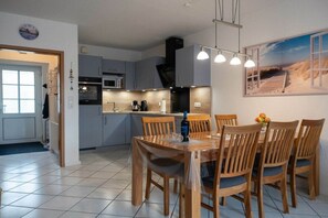 Eine moderne Küche mit grauen Schränken, einem Holztisch und Blick auf den Strand durch ein Fenster.