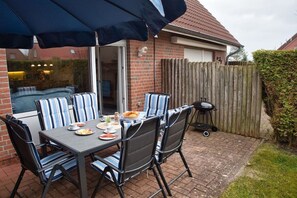 Eine Terrasse im Freien mit Tisch, Stühlen, einem Grill und einem Holenzaun.