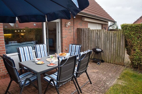 Een terras buiten met een tafel, stoelen, een barbecue en een houten omheining.
