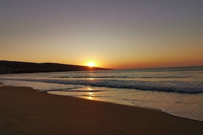 Ein Strand mit Sonnenuntergang über dem Meer, sanfte Wellen spülen ans Ufer.