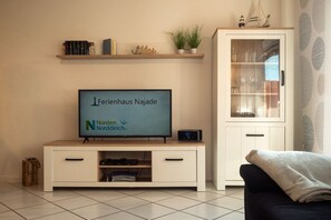 Ein Wohnzimmer mit einem Flachbildfernseher auf einem Holzständer, einer Vitrine und einem dunklen Sofa.
