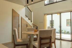 Ein modernes Interieur mit einem Essbereich, der einen runden Tisch und vier Stühle umfasst, einer Treppe mit Holzvertäfelung und einer großen Schiebeglastür zu einem Außenbereich.