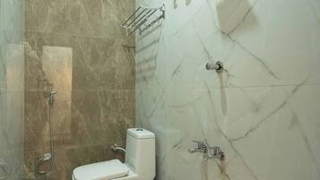 Un baño con inodoro, ducha y una pequeña mesa con un cubo.