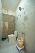 Un baño con inodoro, ducha y una pequeña mesa con un cubo.