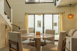 A modern interior with a round table surrounded by chairs, a staircase with wooden railings, and a large sliding glass door leading to an outdoor area. - Howler Monkey Loft (Playas Del Coco)