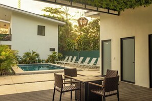 A poolside area with a table and chairs, a pool, and a covered seating area with plants. - Tropical Hideaway Loft (Playas Del Coco)