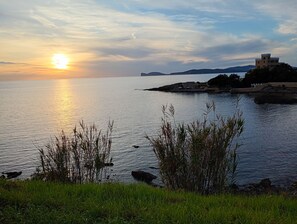 A sunset over a calm body of water with grassy banks and a distant building. - Titilè: a new and comfortable room, surrounded by greenery, with a private entrance (ALGHERO)