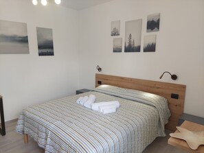A neatly made bed with striped bedding and rolled towels, a wooden headboard, and a nightstand with a lamp. - Titilè: a new and comfortable room, surrounded by greenery, with a private entrance (ALGHERO)