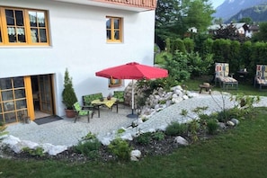 Una casa con un patio amueblado al aire libre, incluyendo un paraguas rojo.