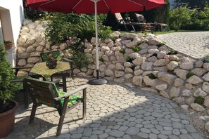 An outdoor patio with a table and chairs, a red umbrella, and a stone wall. - Holiday apartment with 2 bedrooms (Bischofswiesen)