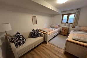 Een slaapkamer met een bank, twee éénpersoonsbedden, een dressoir, een spiegel en een raam met gordijnen.