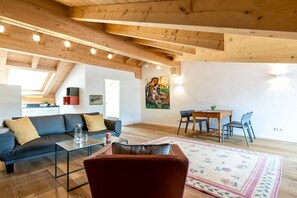 A modern living room with a wooden ceiling, a sofa, a coffee table, and a dining area with chairs and a table. - Holiday apartment with 2 bedrooms (Garmisch-Partenkirchen)