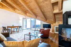 A spacious living area with a high ceiling, a fireplace, a dining table with chairs, and a sofa. - Holiday apartment with 2 bedrooms (Garmisch-Partenkirchen)