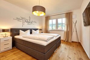 Ein modernes Schlafzimmer mit einem großen Bett, Nachttischen, einer Wandleuchte und einem Fenster mit Vorhängen.