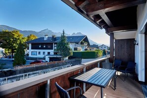 A balcony with a wooden table and chairs, overlooking a residential area with houses and mountains in the background. - Holiday apartment with 2 bedrooms (Garmisch-Partenkirchen)