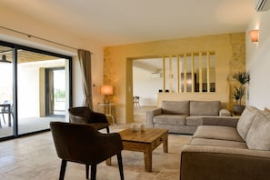 Een ruime woonkamer met een bank, stoelen en een salontafel. Er is een schuifdeur naar een buitenruimte.