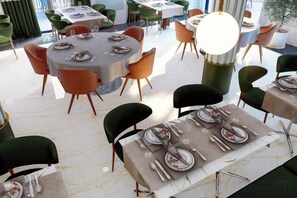 Un restaurante con mesas y sillas redondas, suelo de mármol y una lámpara de araña grande.