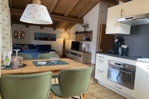 A cozy kitchen with a wooden table, chairs, a built-in oven, and a television. - Holiday apartment with 1 bedroom (Ruhpolding, Deutschland)