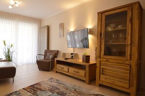 A living room with a sofa, TV, wooden cabinet, and a plant. - Holiday apartment with 2 bedrooms (Norddeich)
