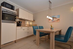 Een moderne keuken met inbouwapparatuur, een eethoek met een tafel en stoelen, en een schilderij aan de muur.